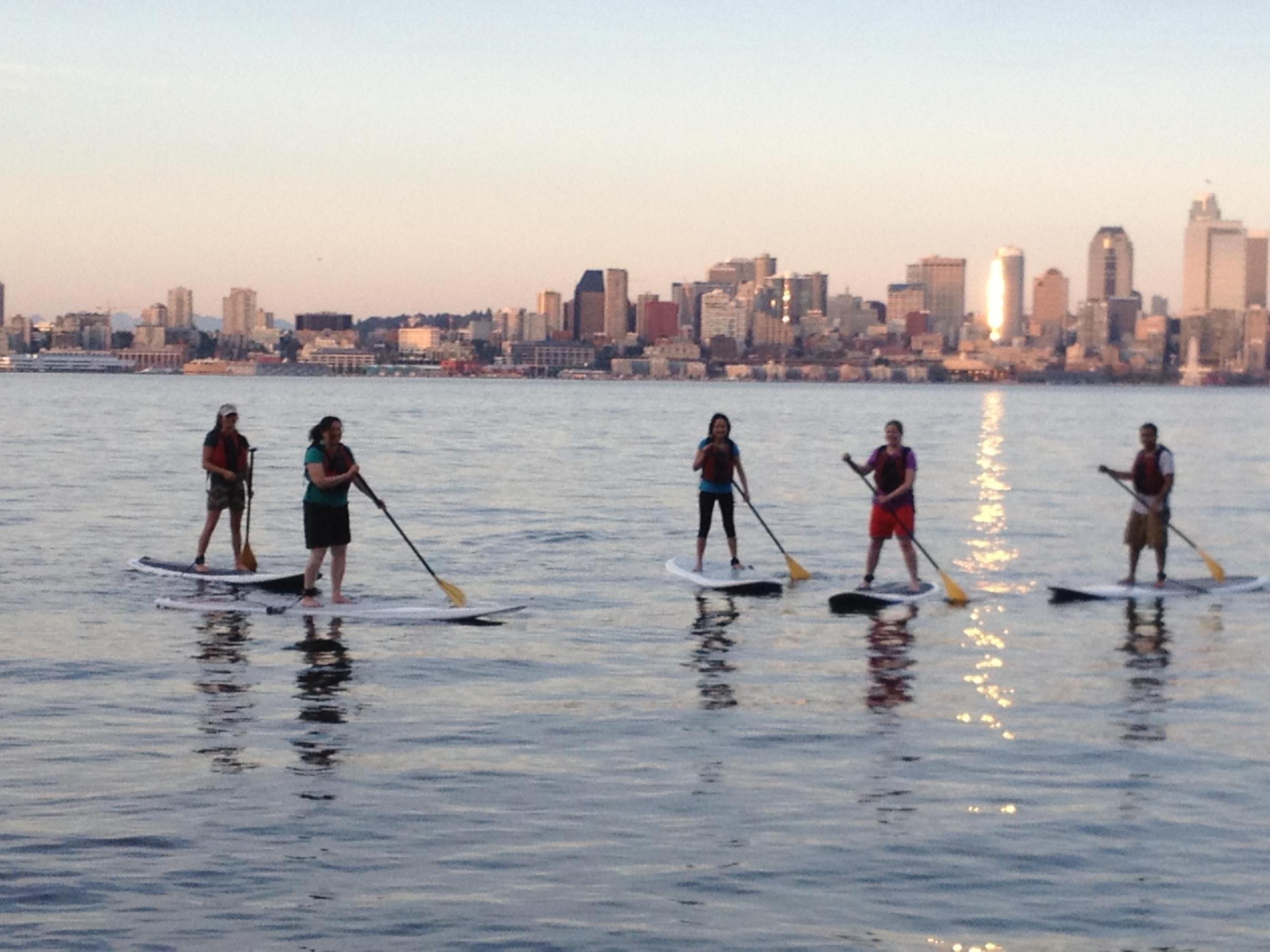 group of stand up paddle boarders in front of Seattle skyline