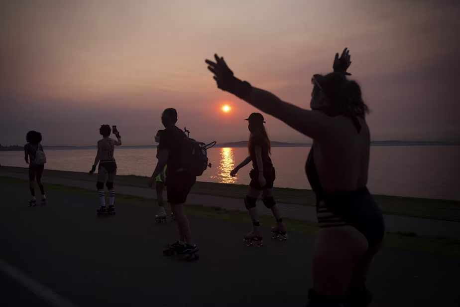 Silhouetted roller skaters on a lakeside path at sunset.